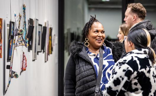 three people talking together in front of art displayed on gallery wall, smiling